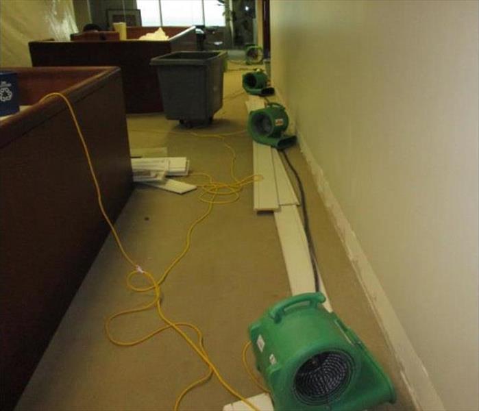 removed baseboards, carpeted floor, green air movers in an office