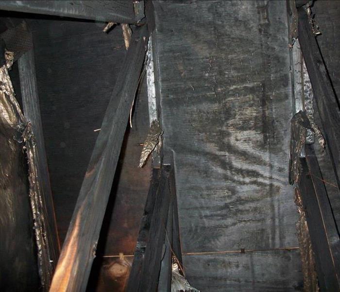 view of blackened attic trusses and sheathing and damaged foil insulation